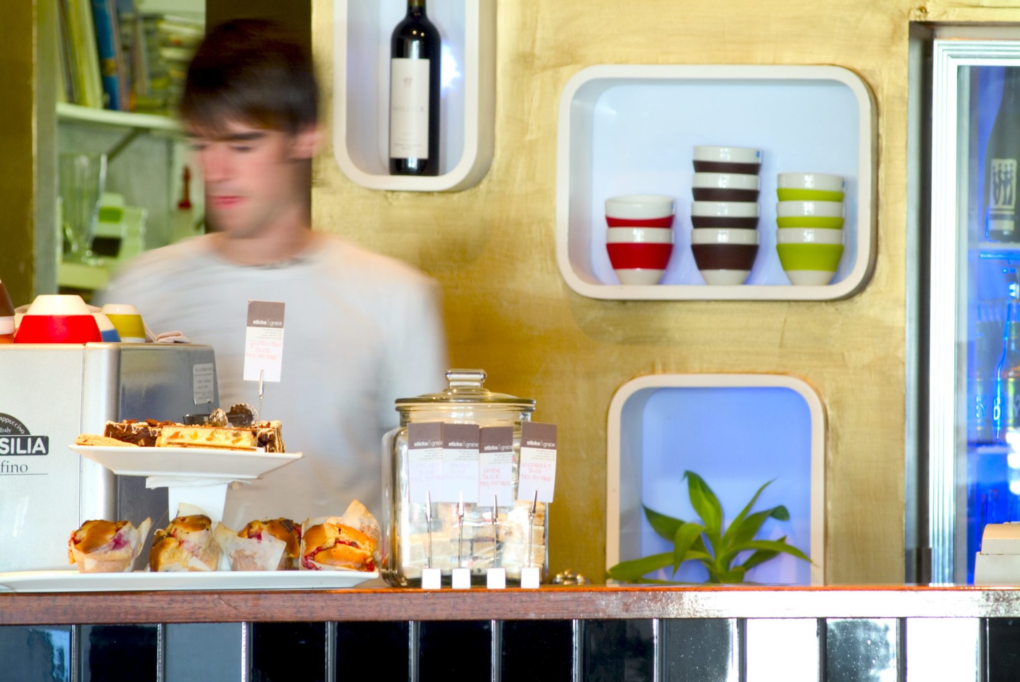 Cafe counter with cakes and coffee maching, with barista face blurred out